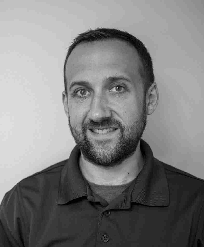 Black and white portrait of a person with short hair and a beard, wearing a polo shirt, smiling slightly against a plain background, exuding confidence in their career.