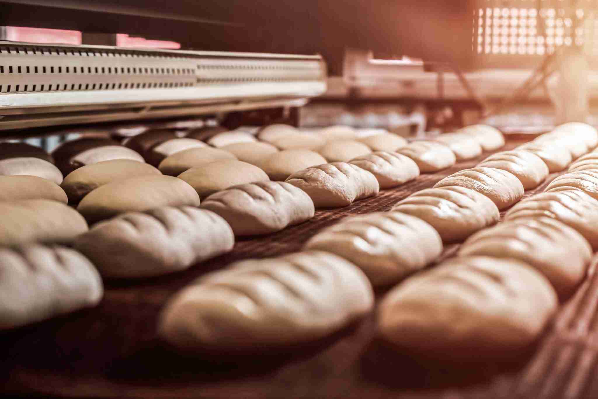 Rows of bread loaves baking inside an industrial oven with a warm, golden light illuminating the scene, highlighting the rising doughs texture—an artful process that parallels the precision in food & beverage water treatment.