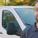 A person stands outdoors in front of a white van labeled Chemstar Water, specializing in mining water treatment. Clad in a dark polo shirt featuring the company logo, they are framed by trees adorned with autumn foliage.