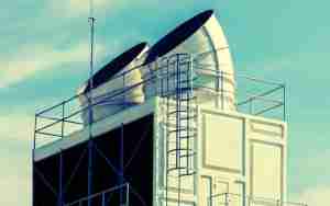 Rooftop cooling tower with large white ducts and black openings, optimized for approach temperature efficiency, surrounded by a metal frame and ladder against a clear blue sky.
