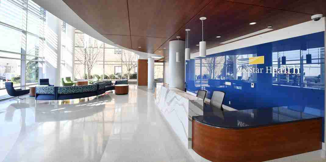 Water Treatment Solutions for Healthcare Facilities - MedStar Southern Maryland Hospital - Commercial Water Treatment - A modern, spacious hospital lobby with a curved wooden ceiling, white floors, reception desk, and blue accent wall with MedStar Health signage—showcasing the importance of Hospital Water Treatment for a safe and welcoming healthcare environment.