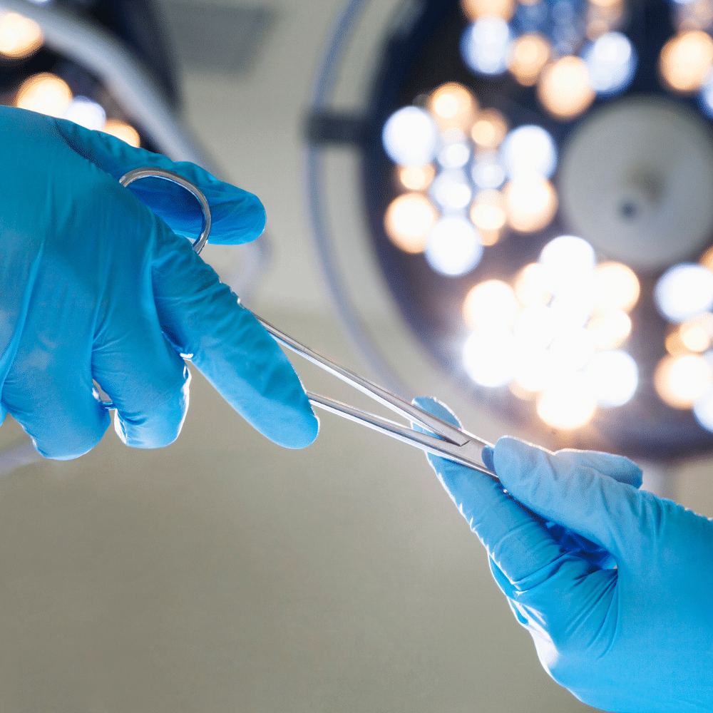 Two hands in blue surgical gloves pass surgical scissors under bright operating room lights, reflecting not only precision in surgery but also the importance of water treatment solutions for healthcare facilities to maintain a sterile environment.