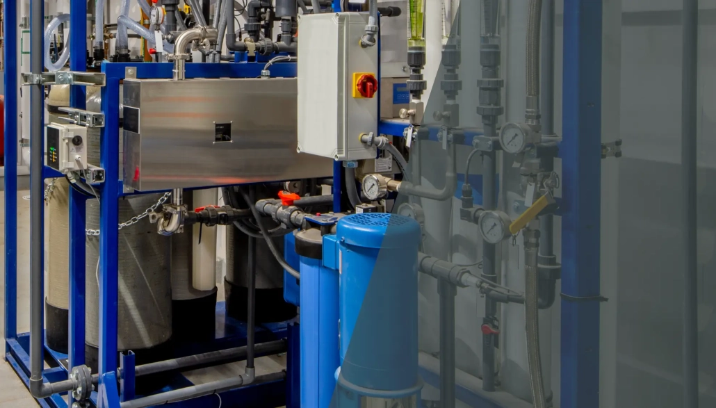 Industrial water filtration system with blue pipes, control panels, gauges, and valves inside a facility, showing equipment used for water treatment or purification processes.