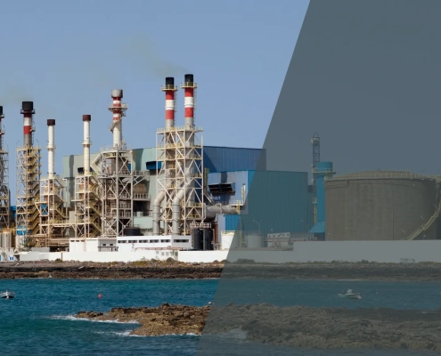 A large industrial desalination plant with multiple smokestacks stands by the sea. The left side is clear and colorful, while the right side is dimmed with a grey overlay. Several boats are visible on the water.