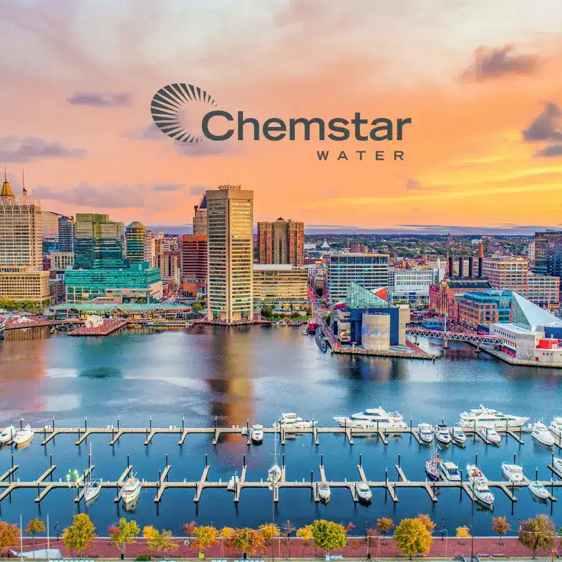 A vibrant sunset over a city harbor with tall buildings, boats docked at a marina, and the Chemstar Water logo overlayed in the sky.