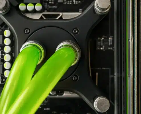 Close-up view of a computers liquid cooling system with two bright green tubes connected to a black component, surrounded by circuit board elements and heatsinks.