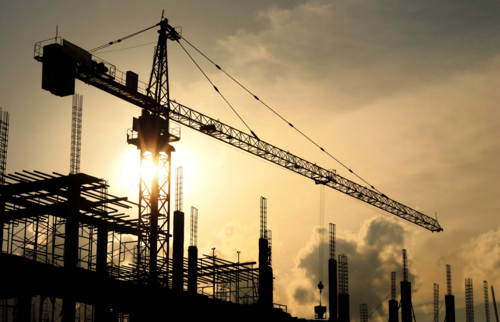 A large crane stands over a hospital under construction at sunset, with steel beams silhouetted against a cloudy sky—an ideal setting to implement advanced hospital water treatment solutions for healthcare facilities.