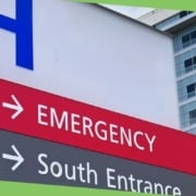A hospital sign with a large blue H and arrows for Emergency and South Entrance stands before a modern healthcare facility, where effective water management and Legionella prevention are crucial to patient safety.